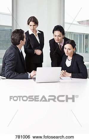 Stock Photograph - Four business people in a meeting using a laptop. Fotosearch
