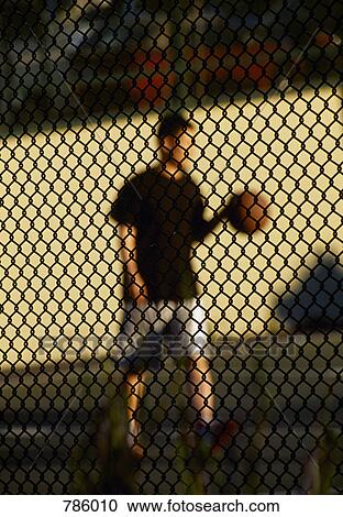 Stock Image - A man playing basketball behind a chainlink fence. Fotosearch