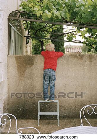 Stock Photo - A boy looking over a patio wall. Fotosearch