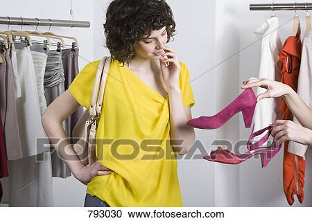 A woman choosing between two shoes in a store View Large Photo Image Stock Image - A woman choosing between two shoes in a store. Fotosearch