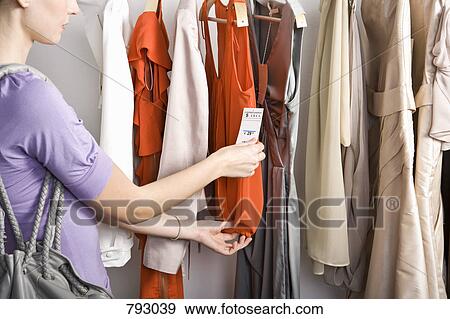 A woman looking at the price tag of a top on a clothing rail View Large Photo Image Stock Photo - A woman looking at the price tag of a top on a clothing rail. Fotosearch