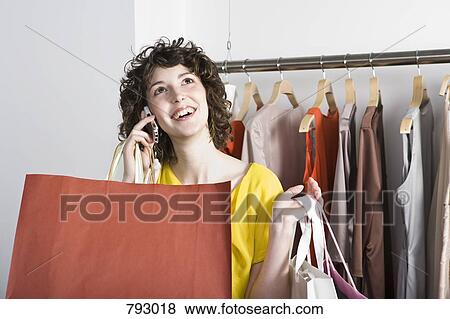 A young woman using her mobile phone in a clothing store View Large Photo Image Stock Photo - A young woman using her mobile phone in a clothing store. Fotosearch