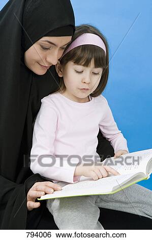 Stock Photograph - A mother wearing a Hijab and her daughter reading a book. Fotosearch
