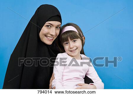 A woman wearing a Hijab and holding her daughter on her lap View Large Photo Image Picture - A woman wearing a Hijab and holding her daughter on her lap. Fotosearch