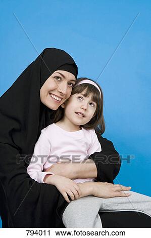A woman wearing a Hijab and holding her daughter on her lap View Large Photo Image Stock Image - A woman wearing a Hijab and holding her daughter on her lap. Fotosearch