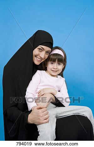 A woman wearing a Hijab and holding her daughter on her lap View Large Photo Image Stock Photo - A woman wearing a Hijab and holding her daughter on her lap. Fotosearch