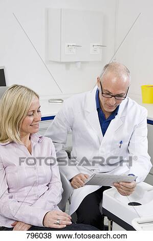 A dentist talking to a patient sitting in a dentist's chair View Large Photo Image Stock Photo - A dentist talking to a patient sitting in a dentist's chair. Fotosearch
