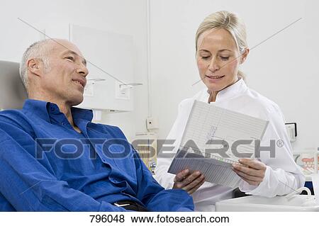 A dentist talking to a patient sitting in a dentist's chair View Large Photo Image Stock Photo - A dentist talking to a patient sitting in a dentist's chair. Fotosearch