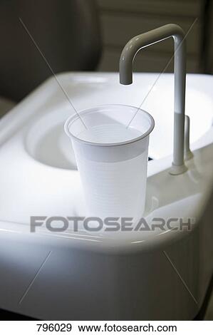 Stock Photo - A plastic cup of water at the edge of a dental cuspidor. Fotosearch