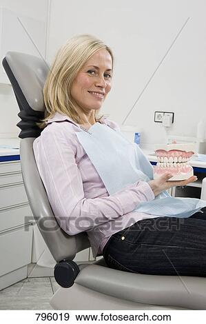 Stock Photo - A woman sitting in a dental chair and holding model teeth. Fotosearch