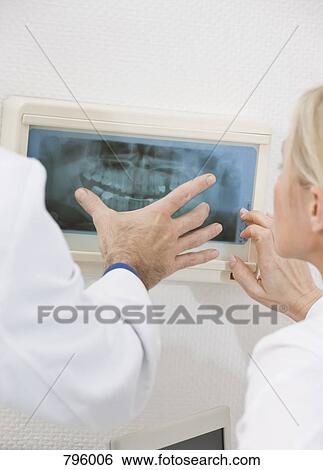 Detail of a dentist and a dental assistant looking at an X-ray View Large Photo Image Stock Photograph - Detail of a dentist and a dental assistant looking at an X-ray. Fotosearch