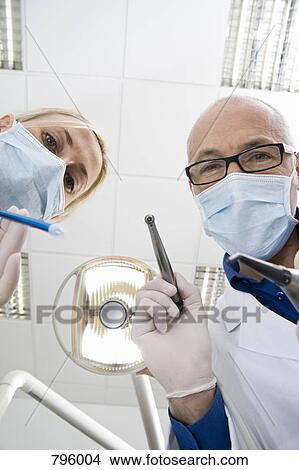 View from below of a dentist and an assistant holding dental tools View Large Photo Image Picture - View from below of a dentist and an assistant holding dental tools. Fotosearch