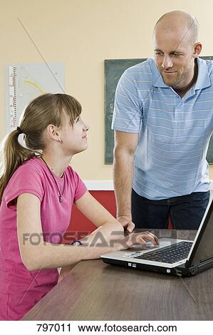 A schoolgirl using a laptop with a teacher standing beside View Large Photo Image Stock Image - A schoolgirl using a laptop with a teacher standing beside. Fotosearch
