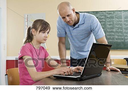 A schoolgirl using a laptop with a teacher standing beside View Large Photo Image Stock Photo - A schoolgirl using a laptop with a teacher standing beside. Fotosearch