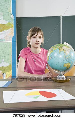 Stock Photo - Portrait of a schoolgirl sitting near a globe. Fotosearch