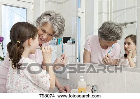 Picture - A grandmother helping her granddaughter brush her teeth. Fotosearch