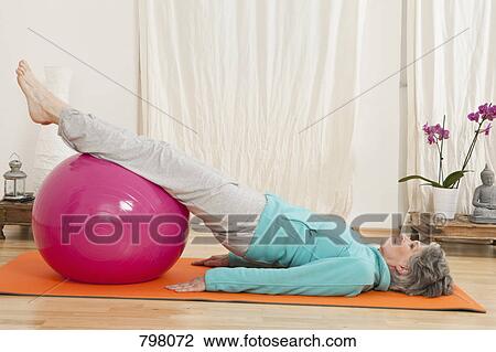 Stock Image - A senior woman doing yoga with a fitness ball. Fotosearch