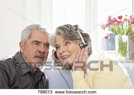Stock Image - A senior woman sharing her headphones for a senior man to listen. Fotosearch