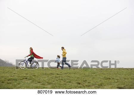 Stock Photo - A boy and a man chasing a woman riding a bike. Fotosearch