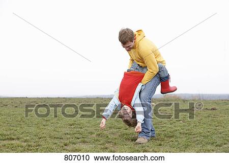 Stock Image - A man holding a boy upside down in a park. Fotosearch