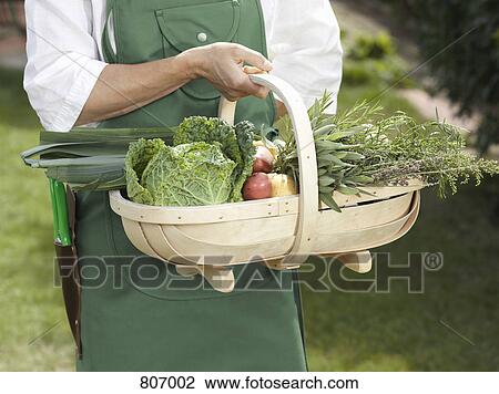 Stock Image - Midsection of a man holding a basket of vegetables. Fotosearch