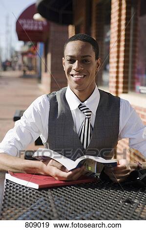 A young man sitting at a pavement cafe and reading books View Large Photo Image Stock Photo - A young man sitting at a pavement cafe and reading books. Fotosearch