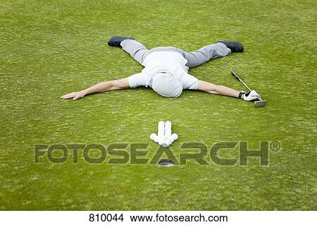 A golfer lying on a putting green behind an arrow of golf balls View Large Photo Image Picture - A golfer lying on a putting green behind an arrow of golf balls. Fotosearch