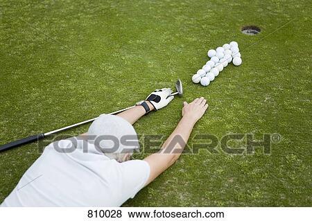 A golfer lying on a putting green behind an arrow of golf balls View Large Photo Image Stock Photo - A golfer lying on a putting green behind an arrow of golf balls. Fotosearch