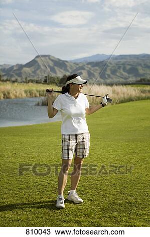 Stock Image - A golfer standing with golf clubs across her shoulders, Palm Springs, California, USA. Fotosearch