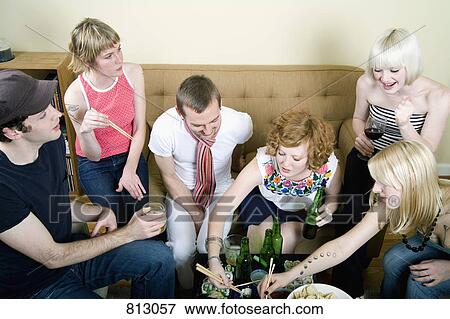 Stock Photo - A group of friends eating and drinking in a living room. Fotosearch