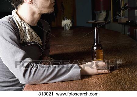 Stock Image - A man sitting at a bar with a bottle of beer. Fotosearch