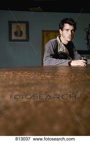 A young man sitting at a bar counter with a drink View Large Photo Image Stock Photo - A young man sitting at a bar counter with a drink. Fotosearch