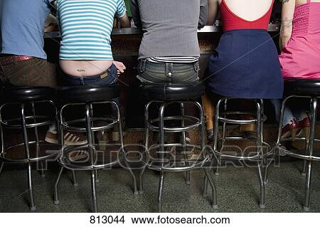 Rear view of a row of friends sitting at a bar counter View Large Photo Image Picture - Rear view of a row of friends sitting at a bar counter. Fotosearch