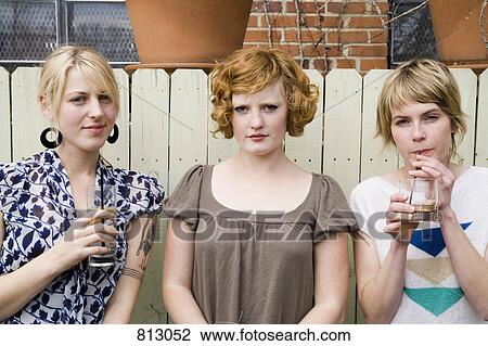 Stock Image - Three young woman standing in front of a fence. Fotosearch