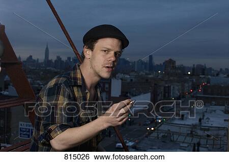Stock Photograph - A young man standing on a fire escape smoking a cigarette. Fotosearch