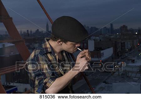 A young man standing on a fire escape lighting a cigarette View Large Photo Image Stock Photograph - A young man standing on a fire escape lighting a cigarette. Fotosearch