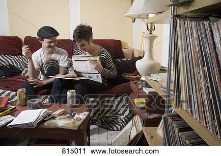 Stock Image - Two young men looking at records on a sofa. Fotosearch