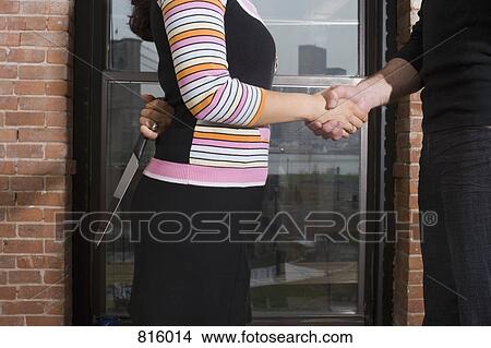 A woman holding a knife behind her back whilst shaking hands View Large Photo Image Picture - A woman holding a knife behind her back whilst shaking hands. Fotosearch