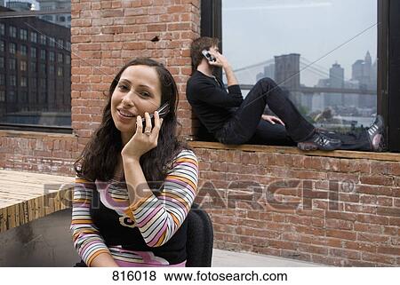 Stock Photo - Two people talking on mobile phones in a modern apartment. Fotosearch