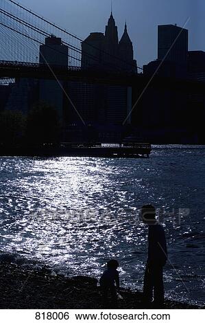 Stock Photograph - Silhouette of people by the East River and the Manhattan skyline, New York City. Fotosearch