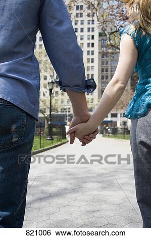 Stock Photograph - A young couple holding hands in a park, Central Park, New York City. Fotosearch
