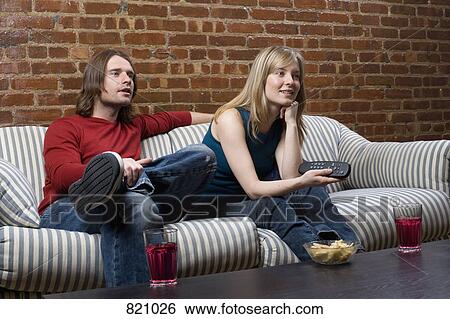Stock Photograph - A young couple sitting on a sofa with a remote control. Fotosearch