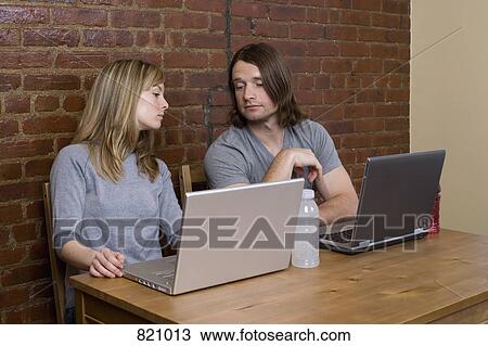 A young couple sitting side by side using laptops View Large Photo Image Stock Image - A young couple sitting side by side using laptops. Fotosearch