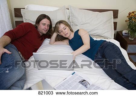 A young couple using a laptop on a bed View Large Photo Image Stock Image - A young couple using a laptop on a bed. Fotosearch