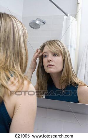 Stock Photography - A young woman looking in a bathroom mirror. Fotosearch