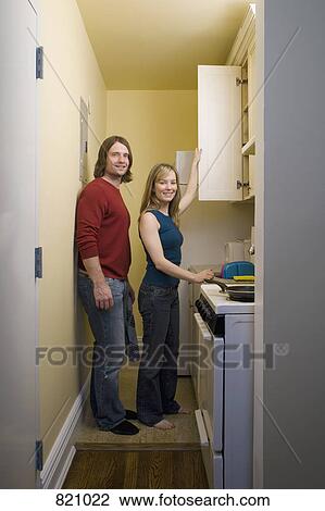 Stock Image - Portrait of a young couple standing in a kitchen. Fotosearch