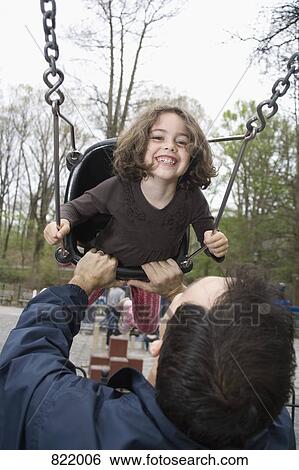 Stock Photograph - A father pushing his daughter on a swing in a park. Fotosearch