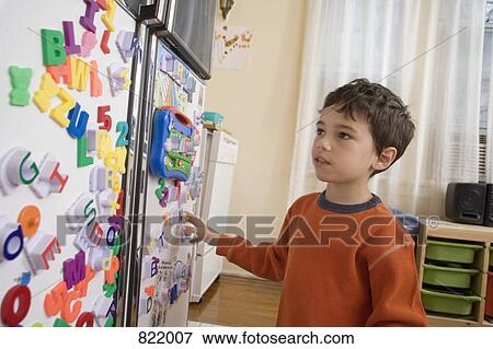 Stock Photo - A young boy looking at toy magnets on a refrigerator door. Fotosearch
