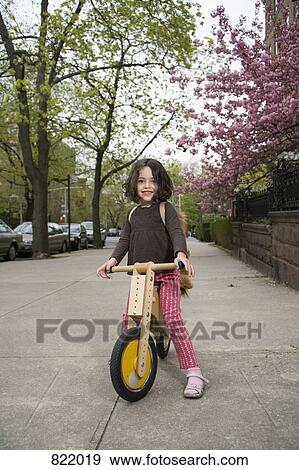 Stock Photo - A young girl on a wooden scooter. Fotosearch