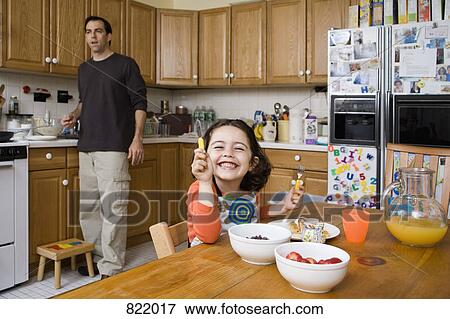 A young girl sitting at a kitchen table and her father standing behind View Large Photo Image Stock Photo - A young girl sitting at a kitchen table and her father standing behind. Fotosearch